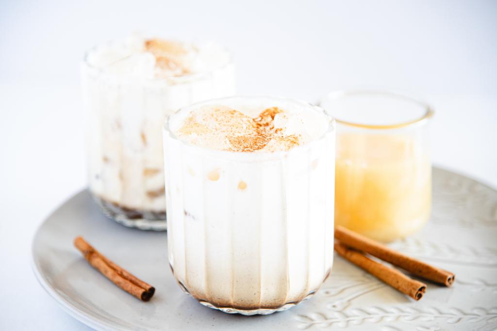 a close up of a honey cinnamon breve on a plate, there are cinnamon sticks on either side of it, and a jar of honey and another breve behind it