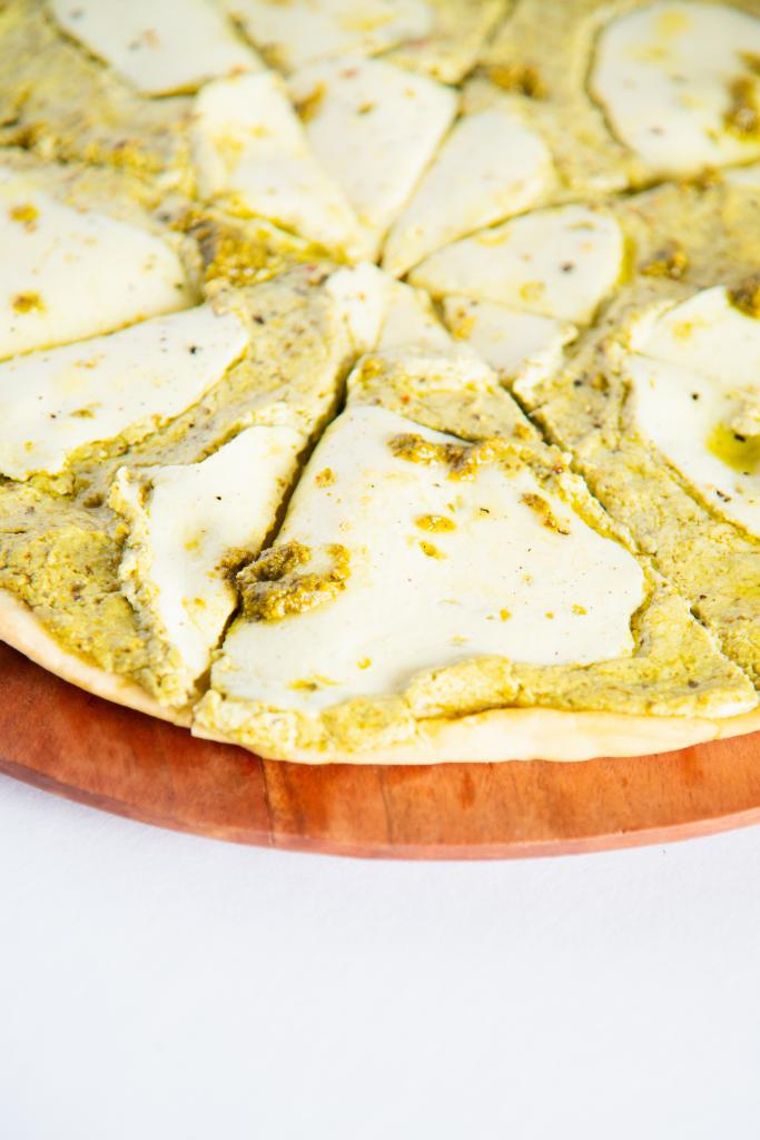 a cut pesto pizza on a wooden cutting board 