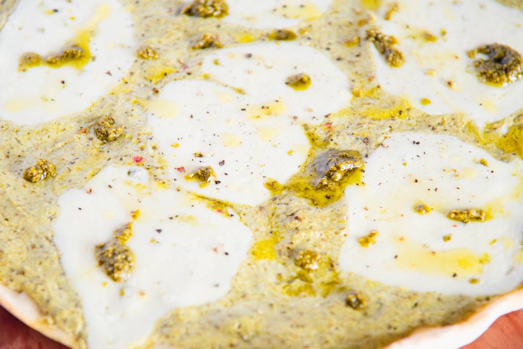 a close up of the top of a finished pesto pizza with olive oil drizzled on top