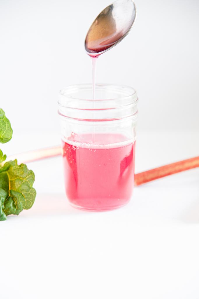 rhubarb syrup running off a metal spoon into a jar of syrup