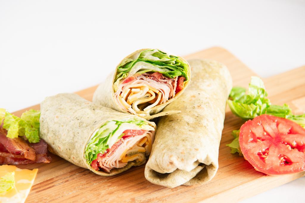 two wraps on a wooden cutting board, one wrap is cut in half so you can see what's inside