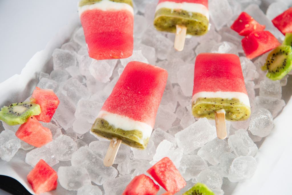 watermelon popsicles on a tray on ice with watermelon chucks and sliced kiwi around them