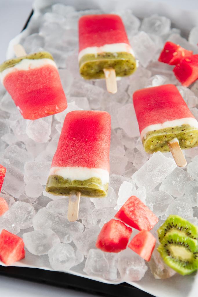 watermelon popsicles on a tray of ice, with some watermelon chucks and sliced kiwi around it 