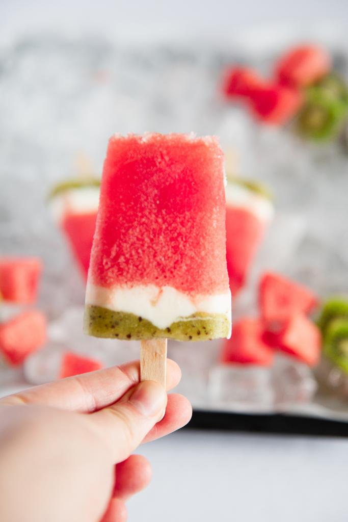 a close up of Popsicle being held in front of a tray of ice with ore watermelon popsicles on it 