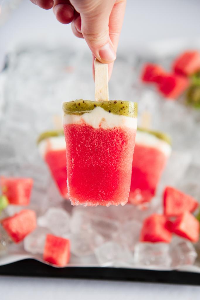 someone holding a popsicle upside down in front of a tray of ice with two other popsicles on it