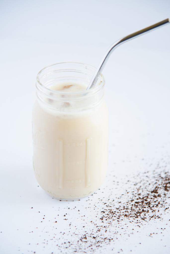 a jar of iced coffee with a metal straw and coffee grounds spilled around it