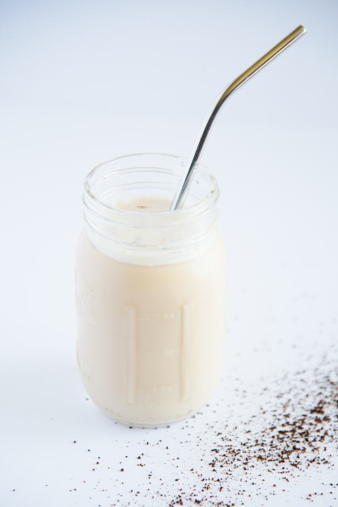 a jar of iced coffee with a metal straw in it, and some coffee grounds spilled around it 