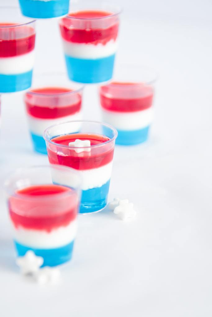 a close up of a jello shot with a white star sprinkle on top, there is another shot in front of it, and some stacked jello shots behind it 