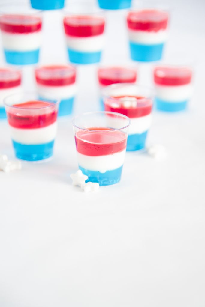 a close up of a jello shot, with more jello shots behind it, and some white star sprinkles around it 