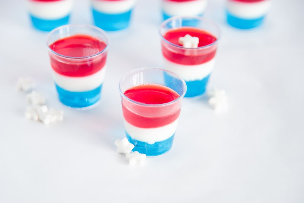 3 jello shots on a table with white star sprinkles around them, one shot has a sprinkle on top of it 