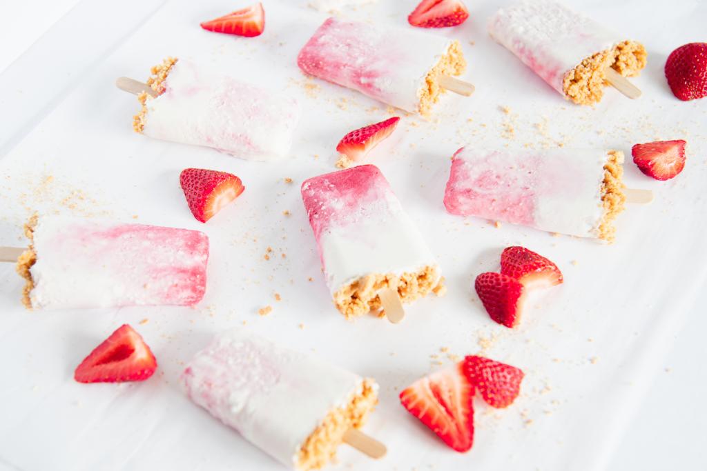 finished strawberry cheesecake popsicles, with chopped strawberry pieces and graham crackers around them