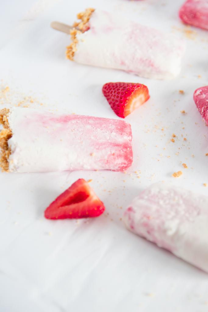 three strawberry cheesecake popsicles with a couple strawberry pieces around it 