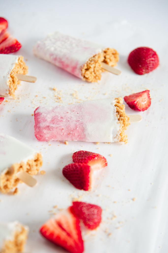 a cheesecake popsicle with chopped strawberries next to it, you can see a few other popsicles in the picture too