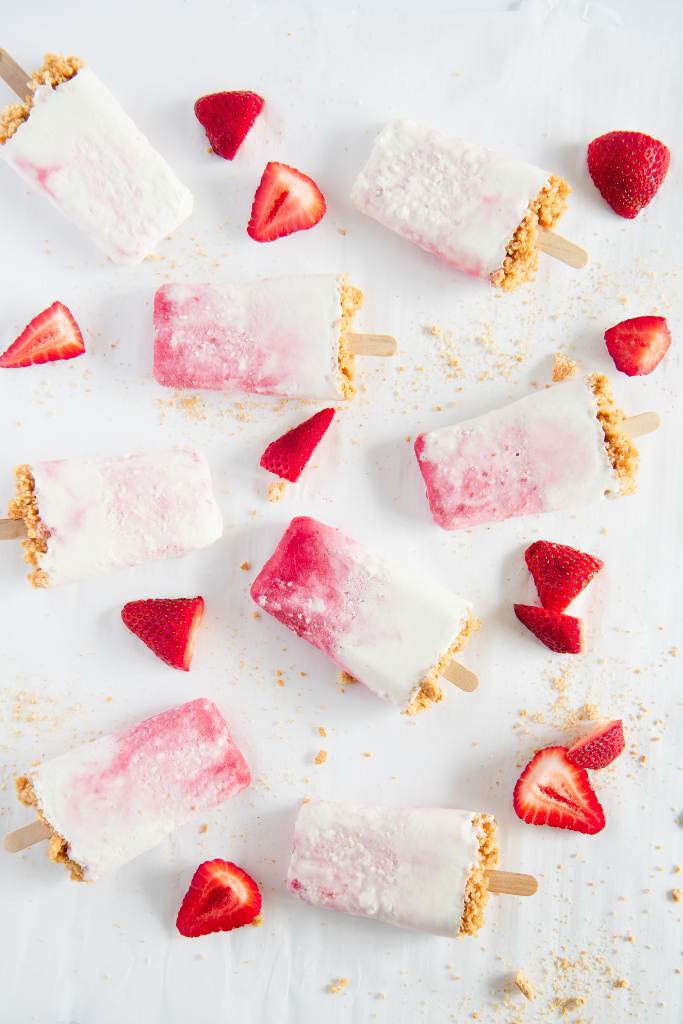 cheesecake popsicles with strawberry pieces and graham cracker crumbs around them 