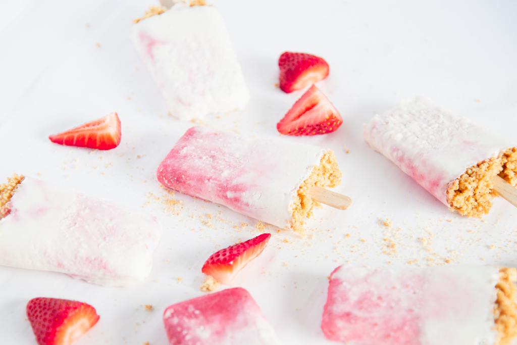 a cheesecake popsicles with chopped strawberries and graham cracker crumbs around it