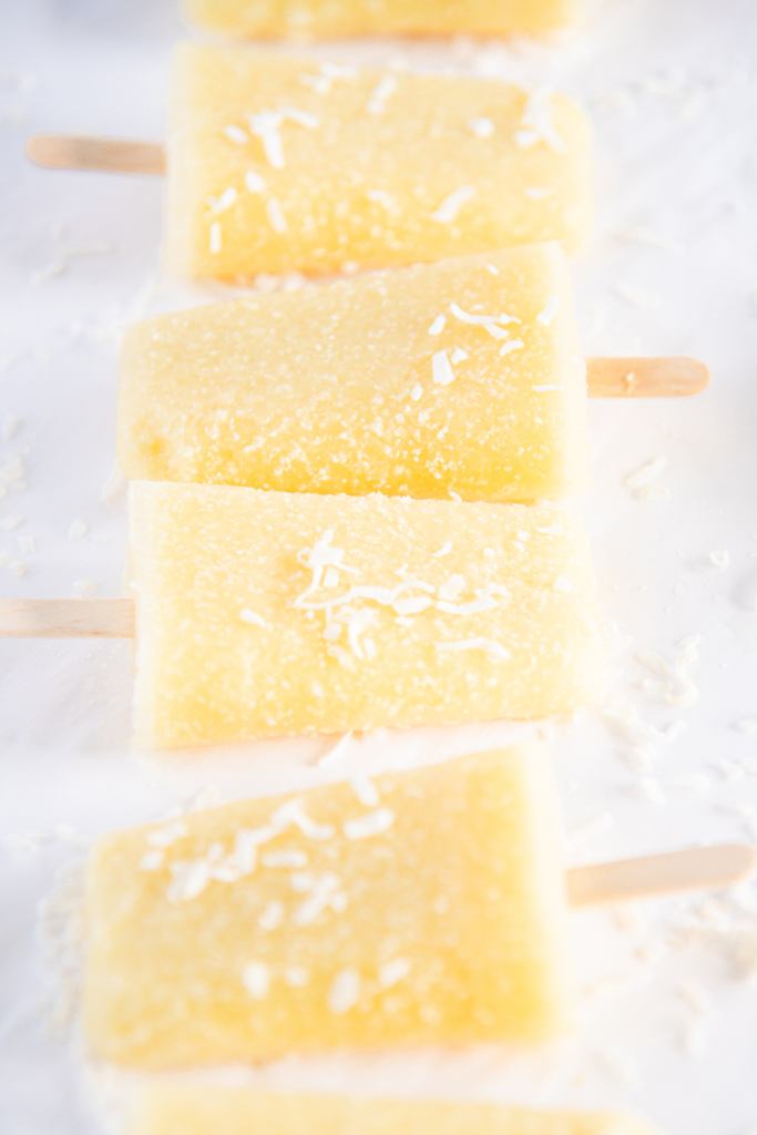 pina colada popsicles in a row with coconut flakes on top of them