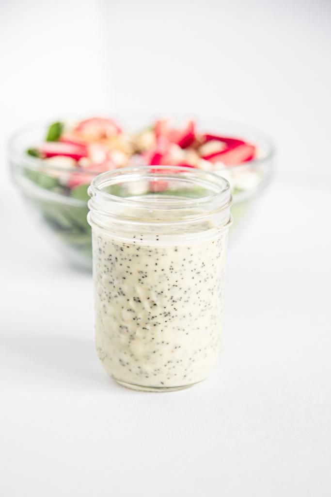 a jar of salad dressing with a bowl of salad behind it 