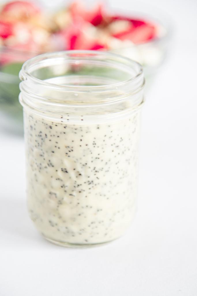 a close up of a jar of salad dressing, with a bowl of salad behind it