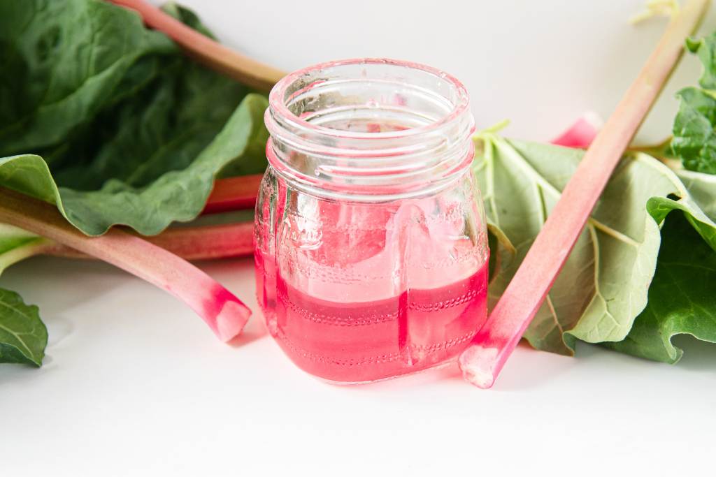 jar of rhubarb syrup with rhubarb stalks around it 