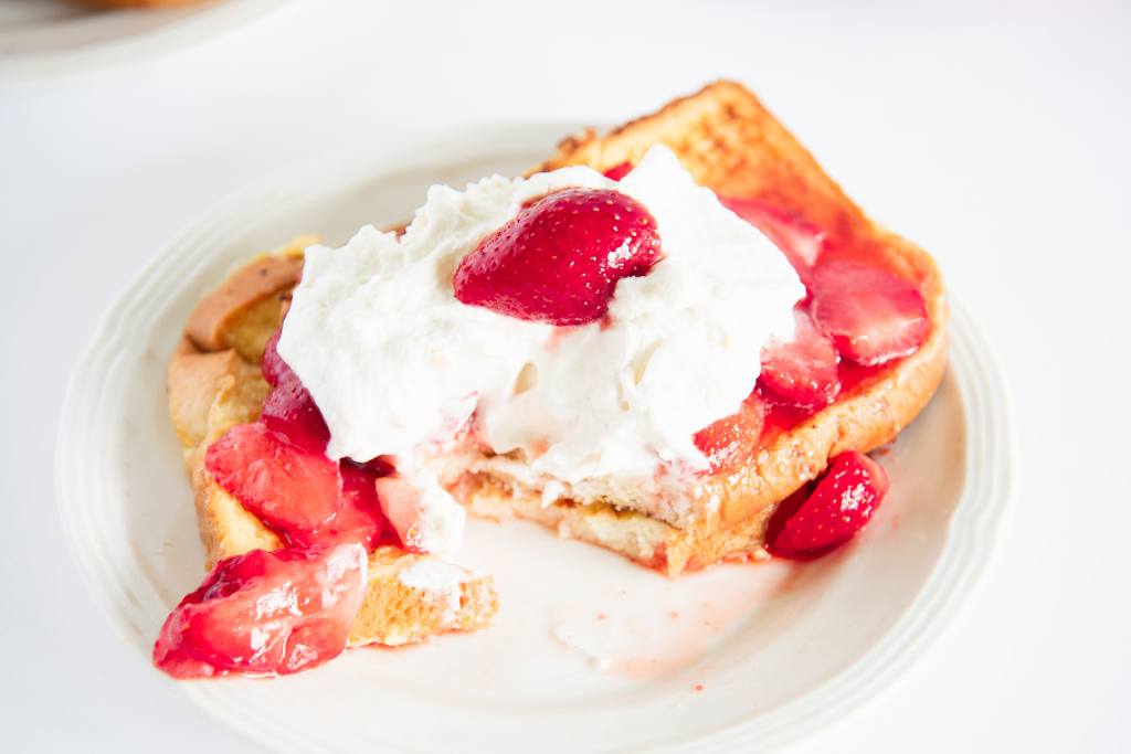 two pieces of french toast with strawberries and whipped cream on top, there is a bite taken out of it 