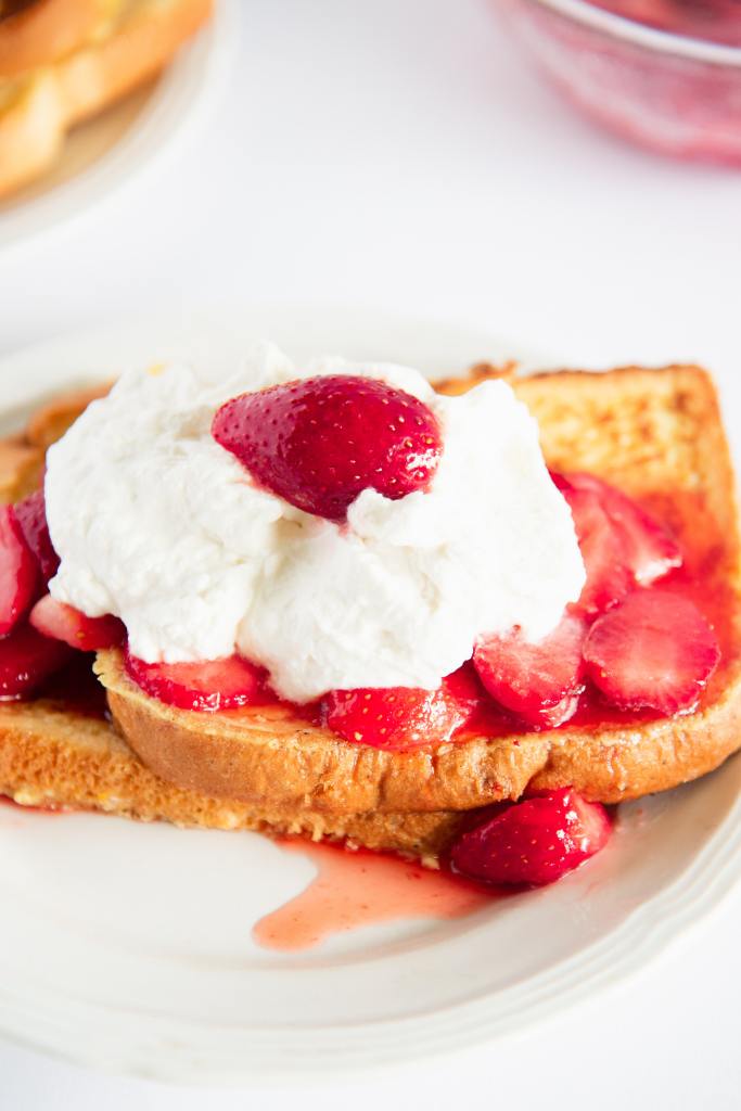 a close up of two pieces of french toast with strawberries and cream on top of them