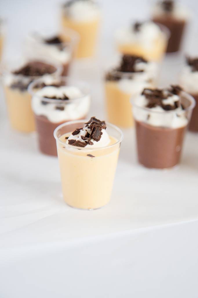 a close up of a vanilla pudding shot with whipped cream and chocolate shavings on top