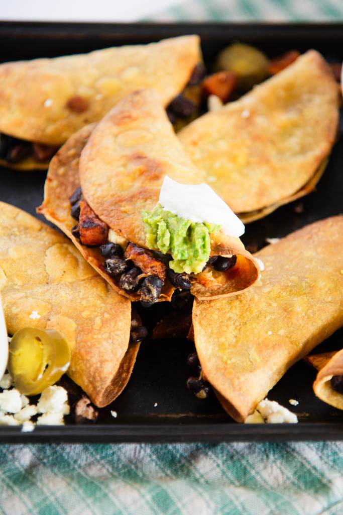 a close up of a crispy taco with sour cream and guacamole on it, on a pan of tacos