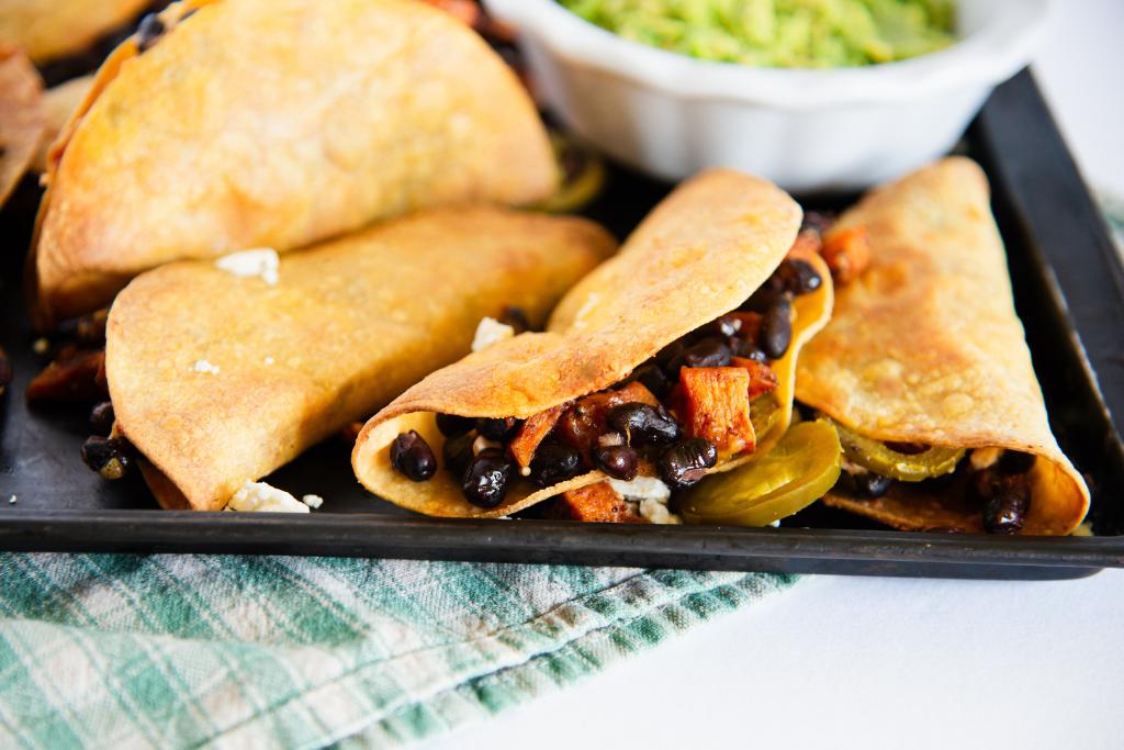 a close up of a taco so you can see the filling, there is a slice of jalapeno next to it, and you can see part of a dish of guacamole behind it