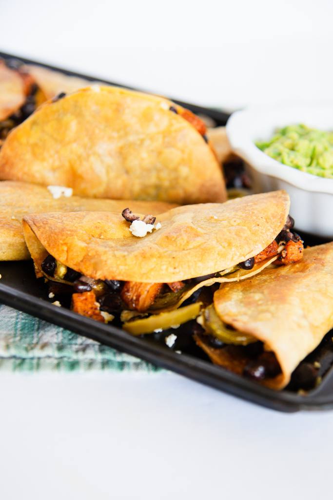 a close up of a pan crispy black bean and sweet potato tacos, you can see part of a dish of guacamole on the pan as well