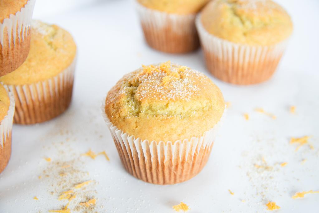 an orange cardamom muffin with sugar and orange zest on it, you are see a few other muffins around it too