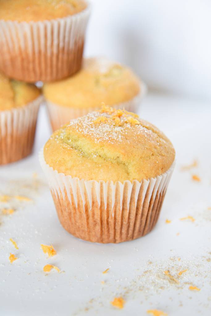 a muffin with orange zest and sugar sprinkled on top, there is a stack of muffins behind it