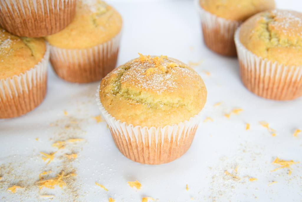 an orange cardamom muffin with sugar on top of it, there are muffins stacked to the side of it with super sprinkled on top