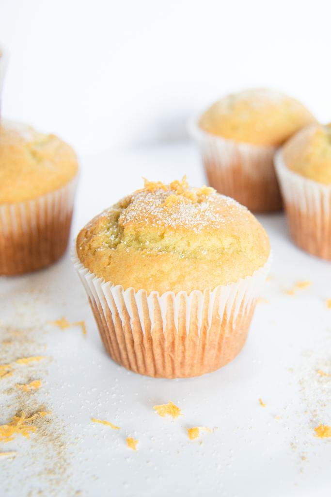 an muffin with sugar and orange zest sprinkled on top of it, there are some muffins behind it as well