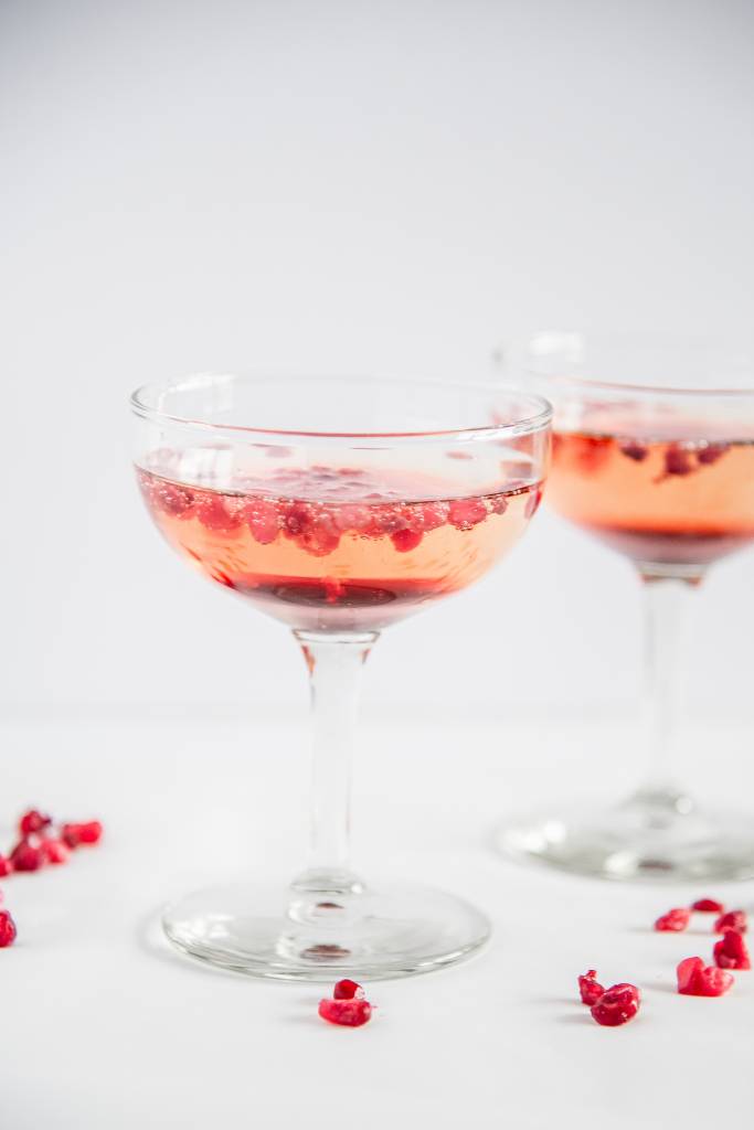 two glasses of champagne with pomegranate seeds floating in it