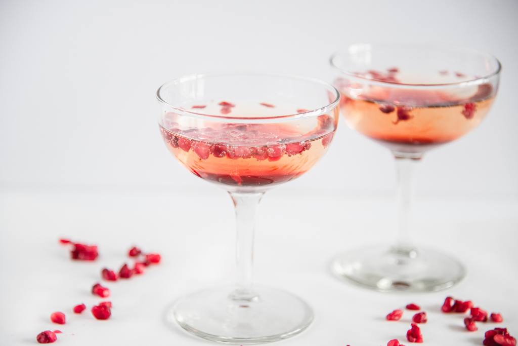 two glasses of pomegranate champagne, there are pomegranate seeds sprinkled around them