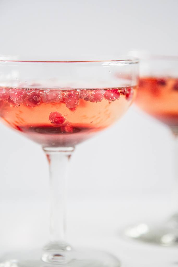 a close up of a pomegranate champagne cocktail, you can see part of another cocktail behind it 