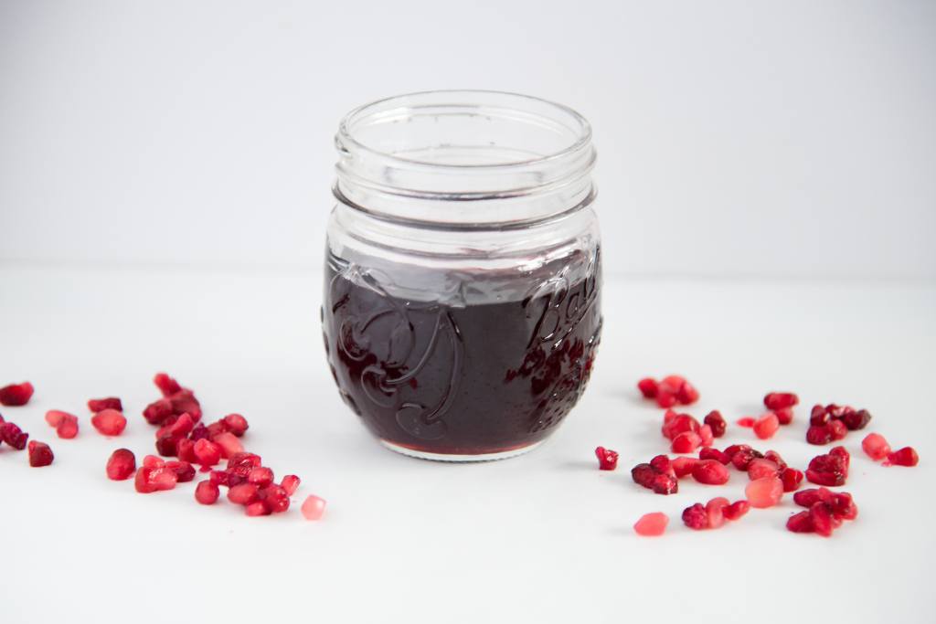 a jar of pomegranate syrup with pomegranate seeds around it