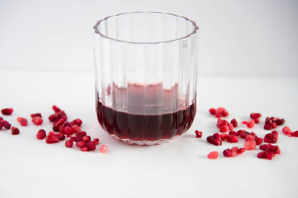 a glass with some pomegranate simple syrup in it, there are pomegranate seeds sprinkled around it