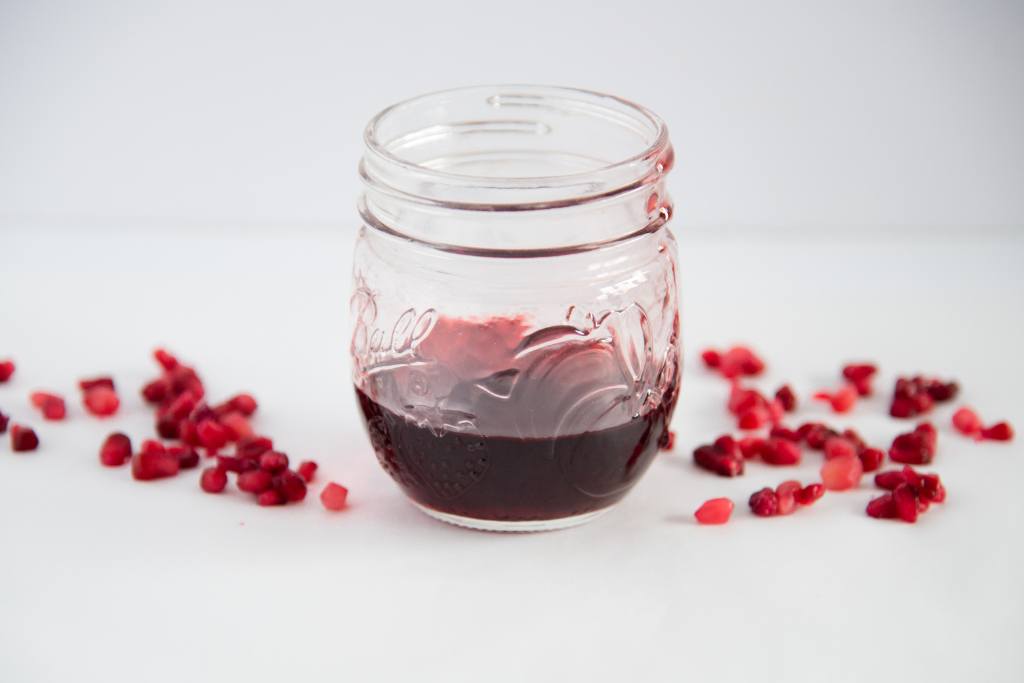 a jar of pomegranate syrup with pomegranate seeds sprinkled around it 