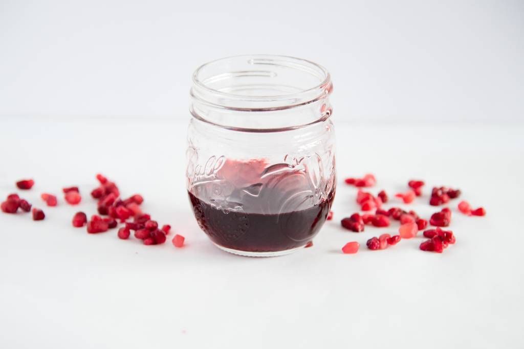 a parochially full jar of pomegranate syrup, with some syrup running down the side 