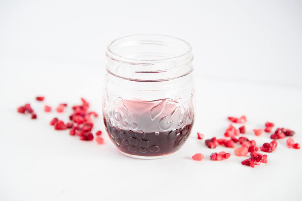 a jar with pomegranate simple syrup and pomegranate seeds around it 