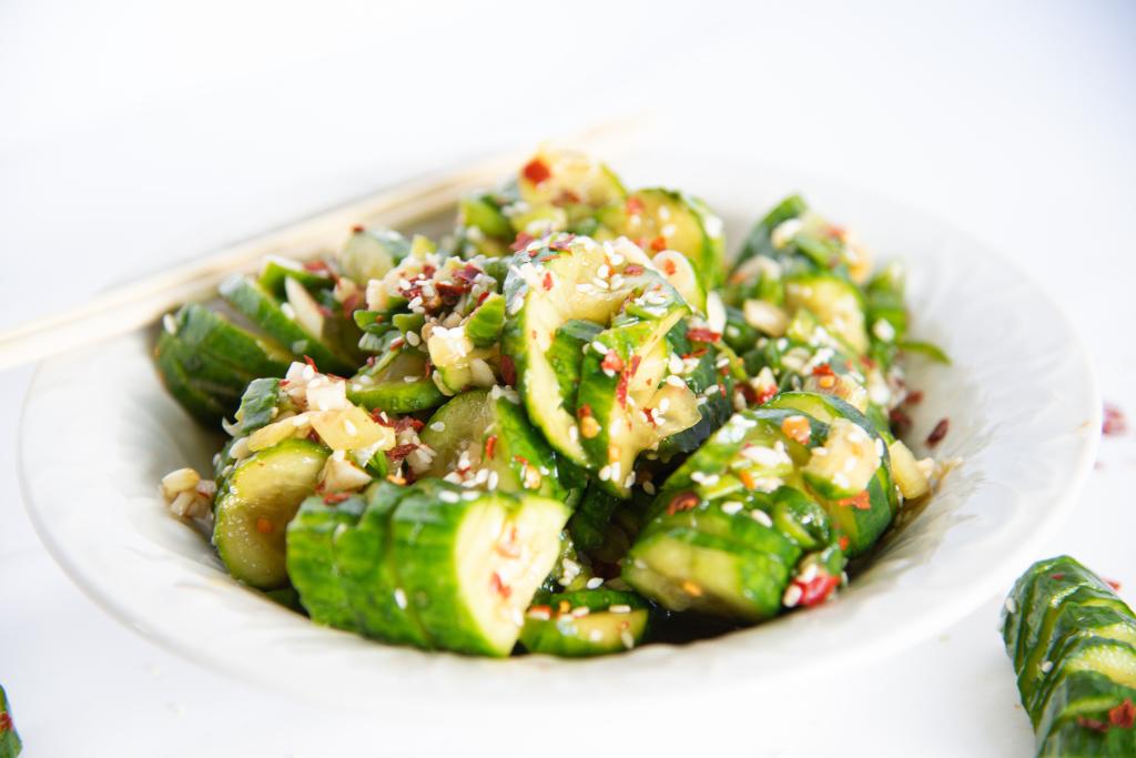 a bowl of spicy cucumber salad with a pair of chopsticks set on the edge of it