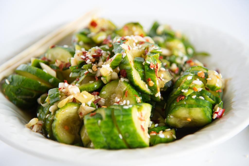 a bowl of cucumber salad with a pair of chopsticks set on the edge