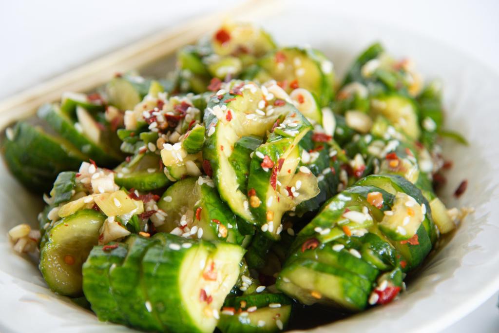 a bowl of spicy cucumber salad with with chopsticks set on the edge of it 