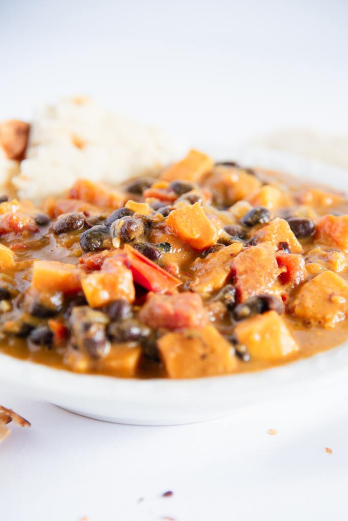 a bowl of sweet potato black bean curry with a piece of naan bread stuck in it 