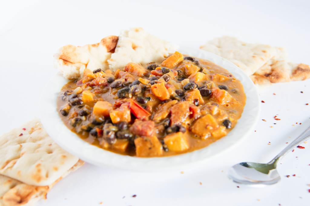 a bowl of curry with a piece of naan bread in it, there is some naan bread and a spoon next to the bowl