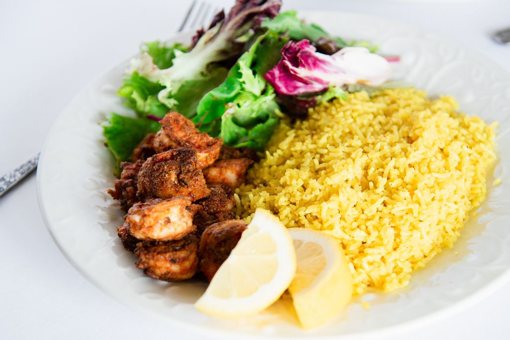 blacked shrimp with rice on a plate, there is also some greens on the plate and two lemon slices