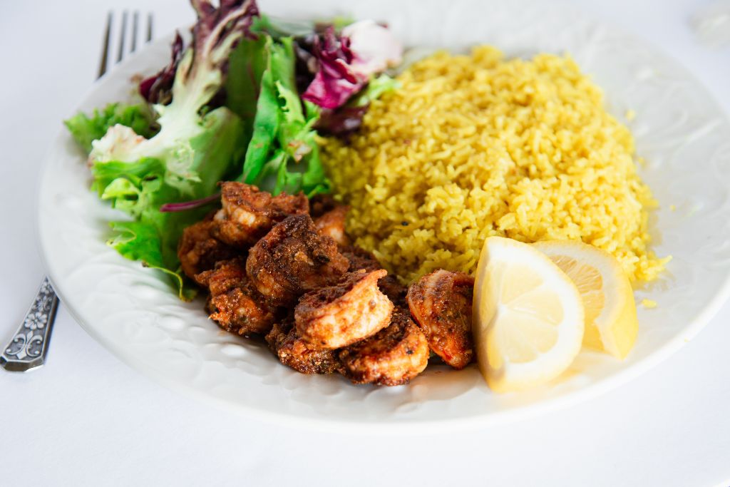 a plate with shrimp, rice, greens, and lemon slices on it, there is also a fork to the left of the plate