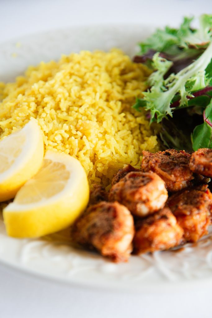 a close up of coconut turmeric rice on a plate, there is also some shrimp, greens and lemon slices on the plate