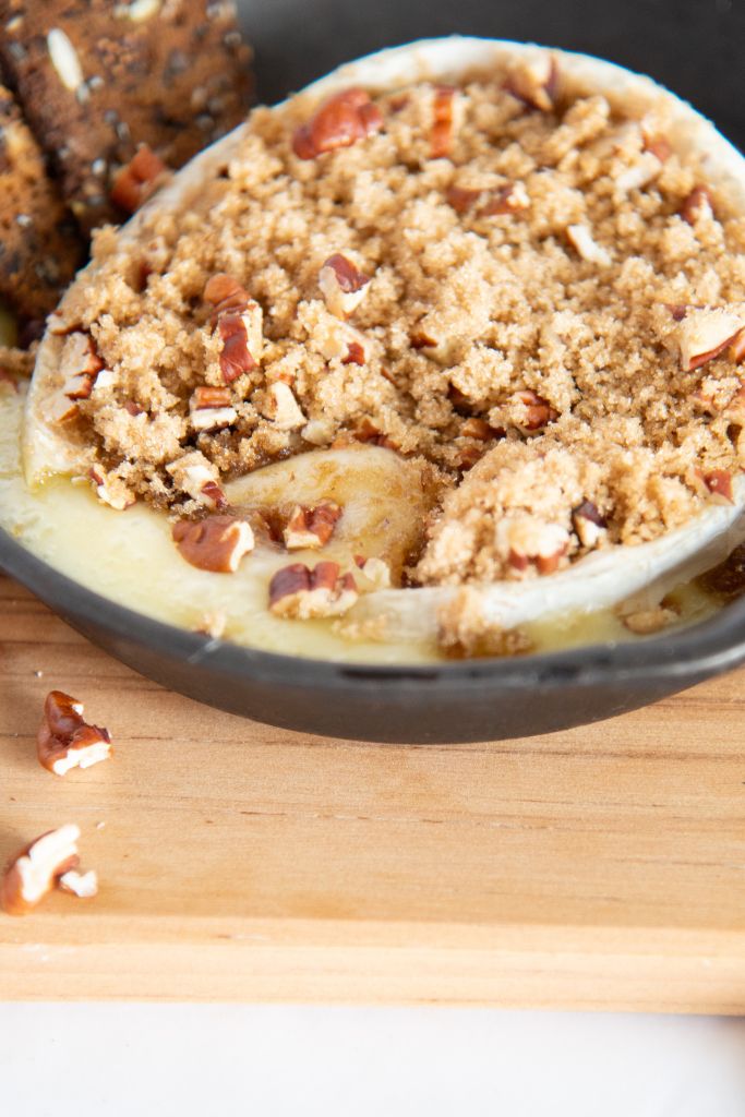 baked brie in a small cast iron skillet, with brown sugar and chopped pecans on top of it.